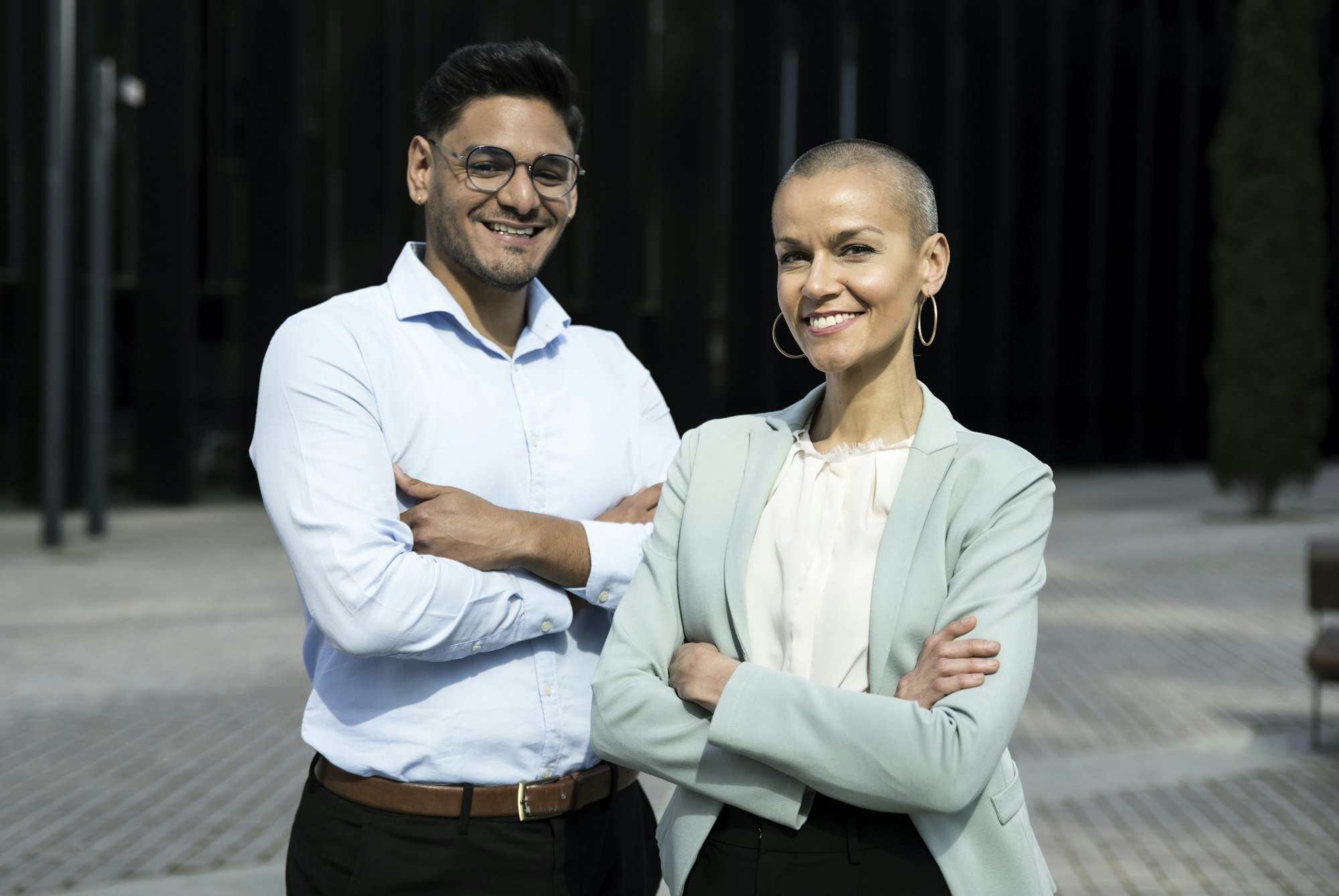 Happy multicultural business couple posing with arms crossed in outdoors. Portrait of multiethnic